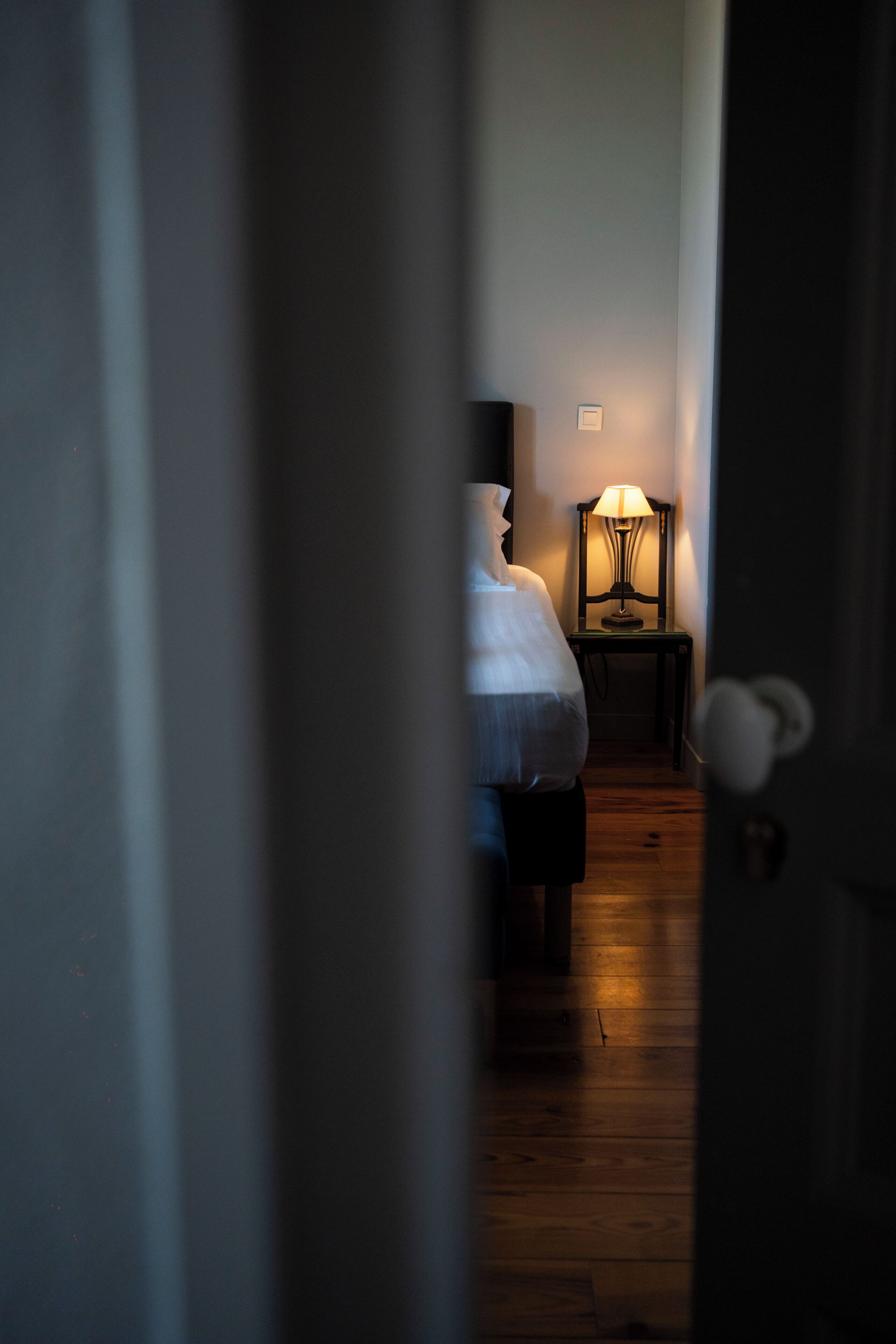 Un couloir étroit mène à une chambre à coucher qui contient un lit et une table de chevet avec une lampe.