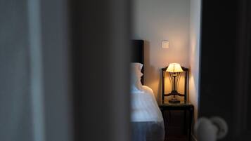 Un couloir étroit mène à une chambre à coucher qui contient un lit et une table de chevet avec une lampe.