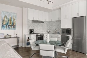 A modern kitchen with white cabinets, stainless steel appliances, and a glass dining table. - Sail Away at The Brent Lofts (Pensacola)