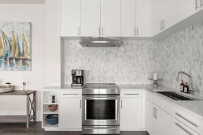 Une cuisine moderne avec des meubles blancs, une hotte de cuisinière en acier inoxydable, un four encastré, une machine à café et un évier avec un robinet.