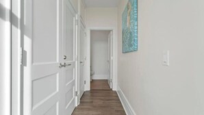Ein Flur mit weißen Türen und Holzboden, der zu einem Badezimmer führt.