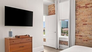 Ein Schlafzimmer mit Bett, Kommode, flachbildfernseher an der Wand und einem Fenster mit Vorhängen.