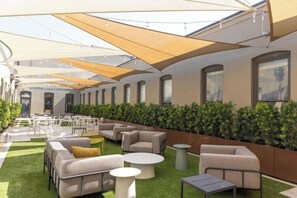 An outdoor seating area with multiple tables and chairs, surrounded by a low hedge and under a series of canopies. - Stunning 1BR Walkable Loft above Palafox (Pensacola)