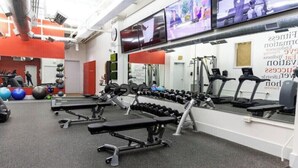 A gym with exercise equipment, a bench, and a wall-mounted TV. - Stunning 1BR Walkable Loft above Palafox (Pensacola)