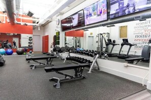 Ein Fitnessraum mit Trainingsgeräten, einer Bank und einem an der Wand montierten Fernseher.
