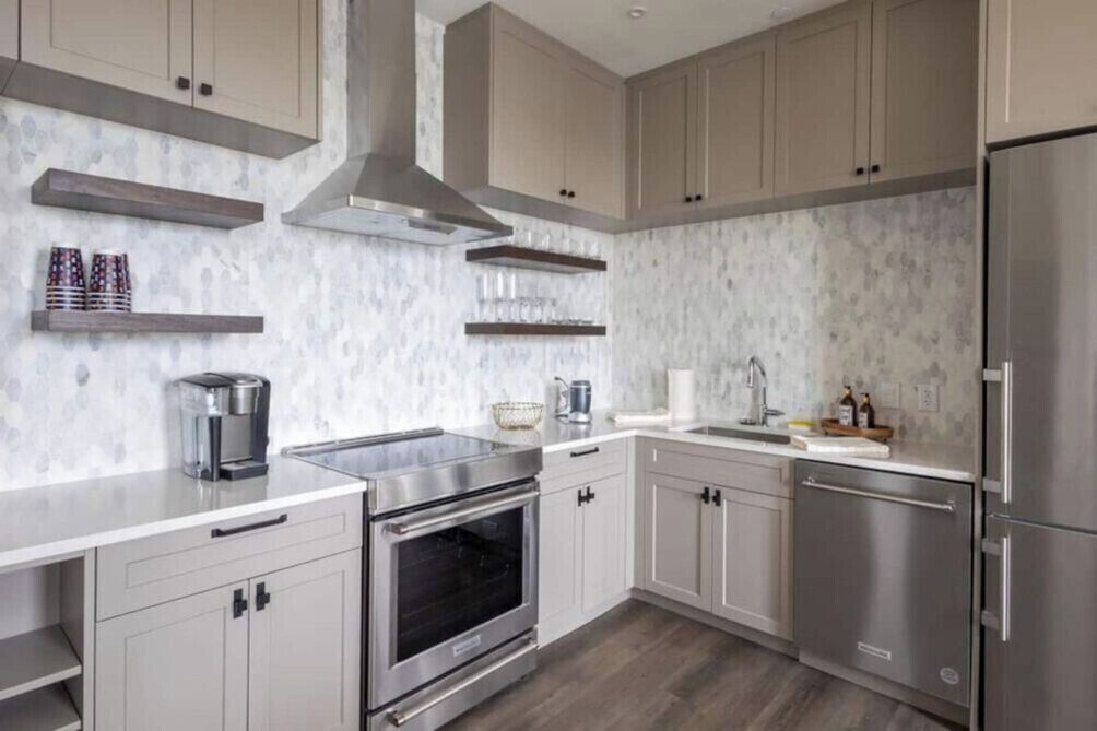 A modern kitchen with stainless steel appliances, light-colored cabinetry, and a marble backsplash.