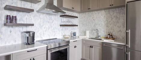 A modern kitchen with stainless steel appliances, light-colored cabinetry, and a marble backsplash.