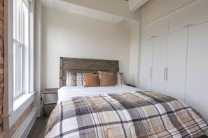 A bedroom with a large bed, a wooden headboard, a window, and a wardrobe. - The Brent Lofts A Quiet Place 303 (Pensacola)