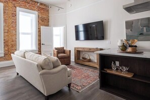 A living room with a sofa, a chair, a TV, and a wooden console table. - Historic Charm Southern Exposure (Pensacola)
