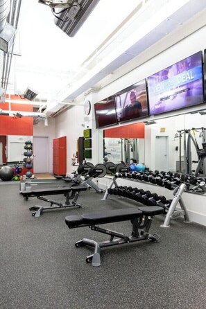 A gym with weightlifting equipment, exercise balls, and a television displaying an advertisement. - Historic Charm Southern Exposure (Pensacola)