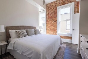 A bedroom with a large bed, a nightstand, a dresser, and a brick wall. - Historic Charm Southern Exposure (Pensacola)