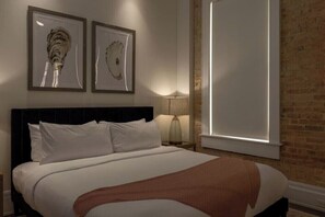 Une chambre d’hôtel avec un grand lit, un mur en briques et deux œuvres d’art encadrées accrochées au mur.