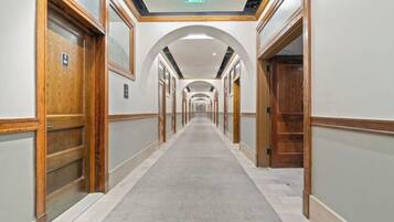 Un couloir d’hôtel avec des portes en bois, une moquette grise et un panneau de sortie au plafond.