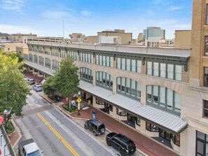 A multi-story building with a row of storefronts on the ground floor, a clear sky, and a street with parked cars. - The Brent Lofts Palafox Penthouse (Pensacola)