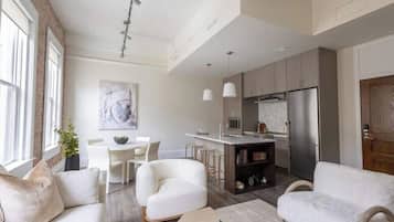 A modern kitchen with a central island, a dining area with a white table and chairs, and a living room with a sofa and a coffee table.
