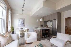 A modern kitchen with a central island, a dining area with a white table and chairs, and a living room with a sofa and a coffee table. - Cotton, Silk, and Linen at the Brent Lofts (Pensacola)