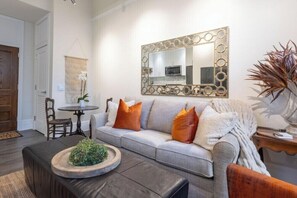 A living room with a sofa, a coffee table, a mirror, and a plant. - Chic Hideaway at the Brent Lofts (Pensacola)