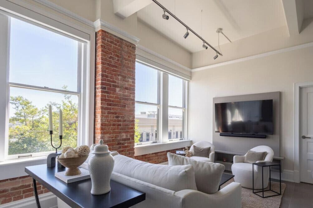 Una sala de estar moderna con chimenea de ladrillo, ventanas amplias, un televisor de pantalla plana y un sofá blanco.