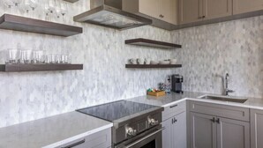 A modern kitchen with a marble backsplash, stainless steel appliances, and built-in shelves. - 2BR Palafox Oasis at the Brent Lofts (Pensacola)