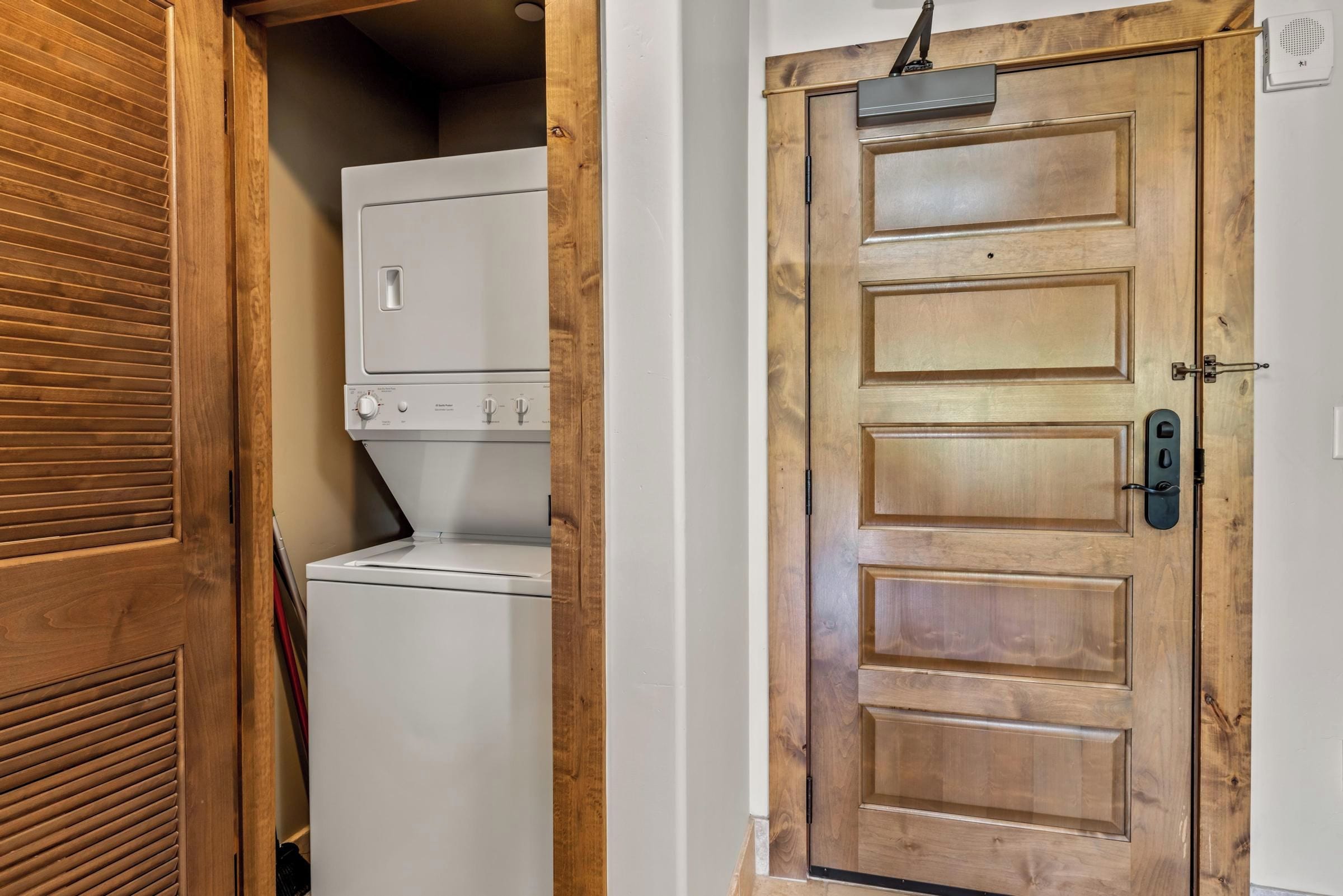 A laundry room with a white washer and dryer, a wooden door with a handle, and a light switch on the wall.