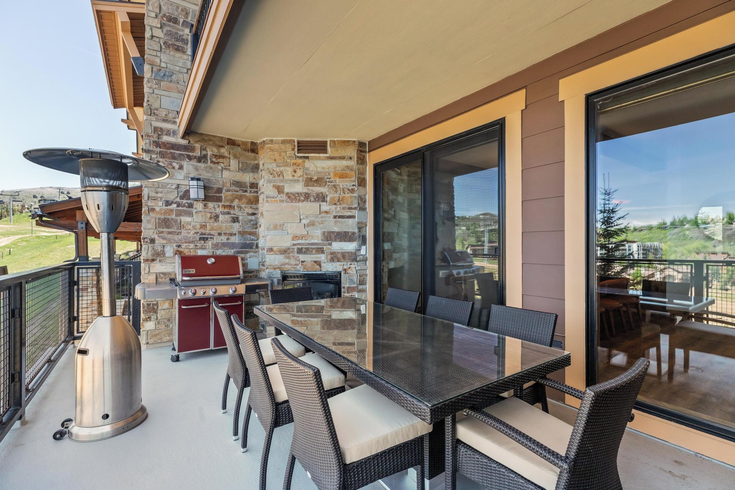 Eine Terrasse im Freien mit einer Steinwand, einem Grill, Korbmöbeln und einem Glastisch.
