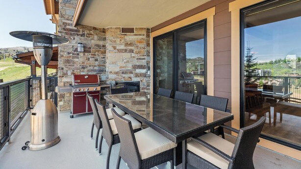 An outdoor patio with a stone wall, a grill, wicker furniture, and a glass table. - Edgemont Condominiums (Steamboat Springs)