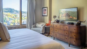 Habitación de hotel con cama, una silla, cómoda, televisor y ventana con vista a un paisaje montañoso.
