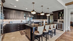 A modern kitchen with dark cabinetry, a central island, bar stools, and pendant lighting. - Edgemont Condominiums (Steamboat Springs)