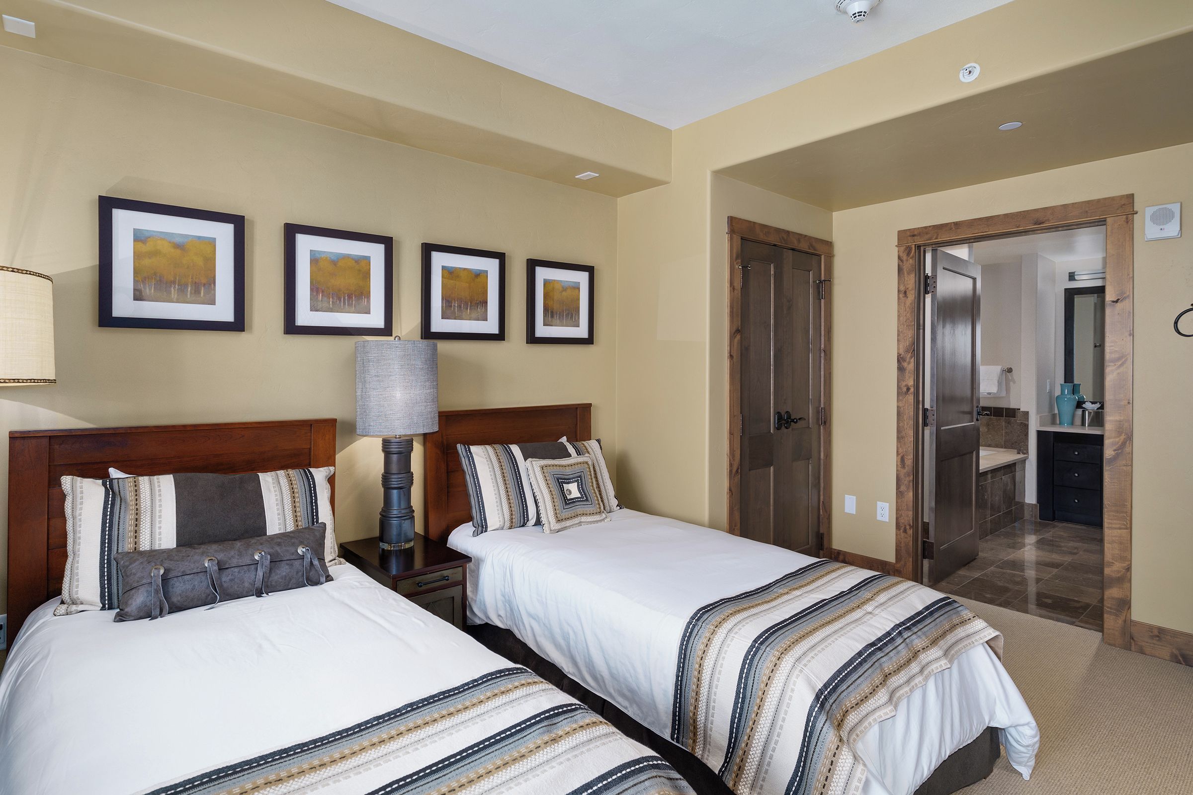 Una camera d'albergo con due letti, un comodino, una lampada e quadri appesi alla parete.