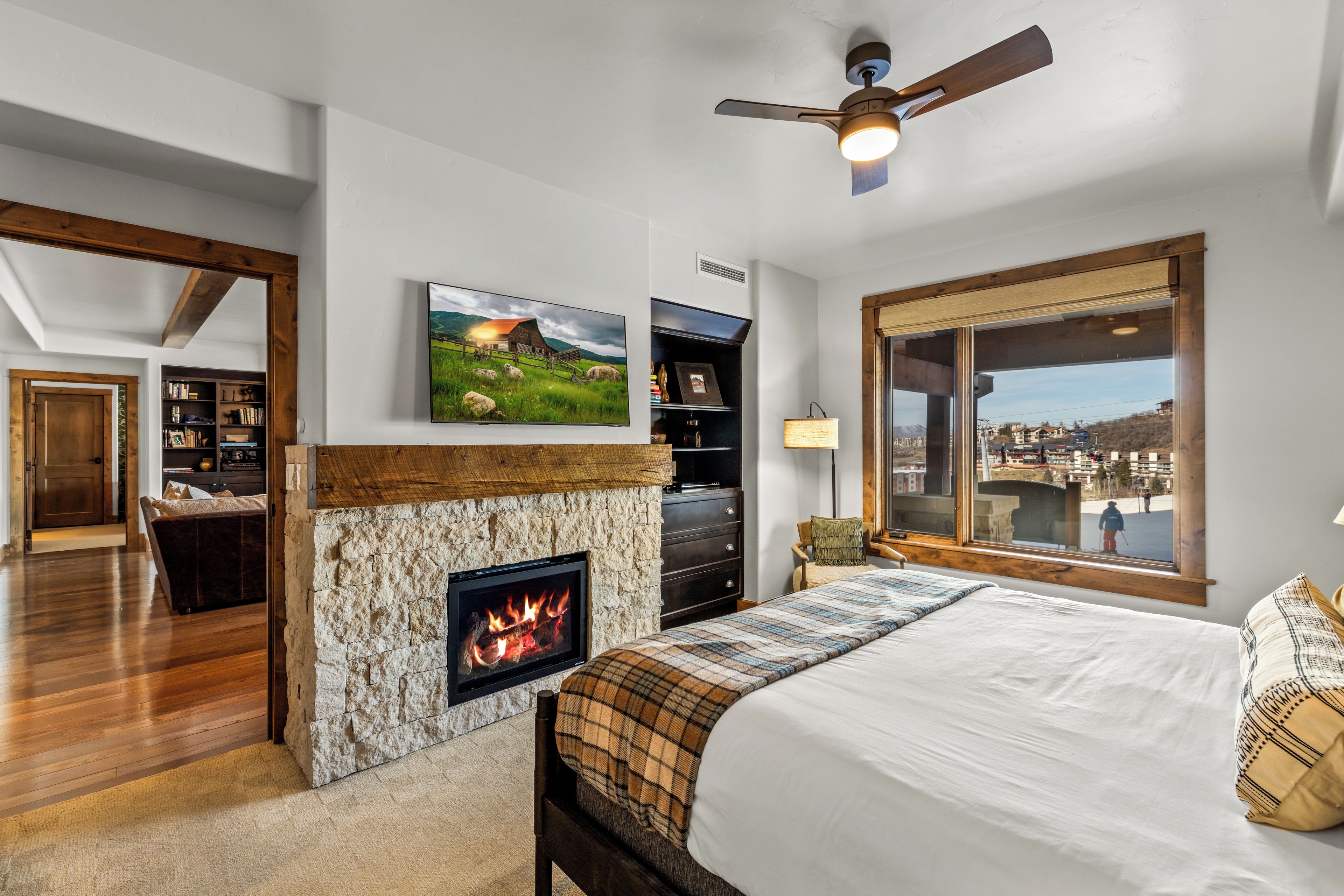 Ein Schlafzimmer mit Kamin, Bett, Fernseher und einem großen Fenster mit Blick.