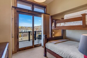 A bedroom with a bunk bed, a large window with a view of a cityscape, and a balcony with outdoor furniture. - Edgemont Condominiums (Steamboat Springs)