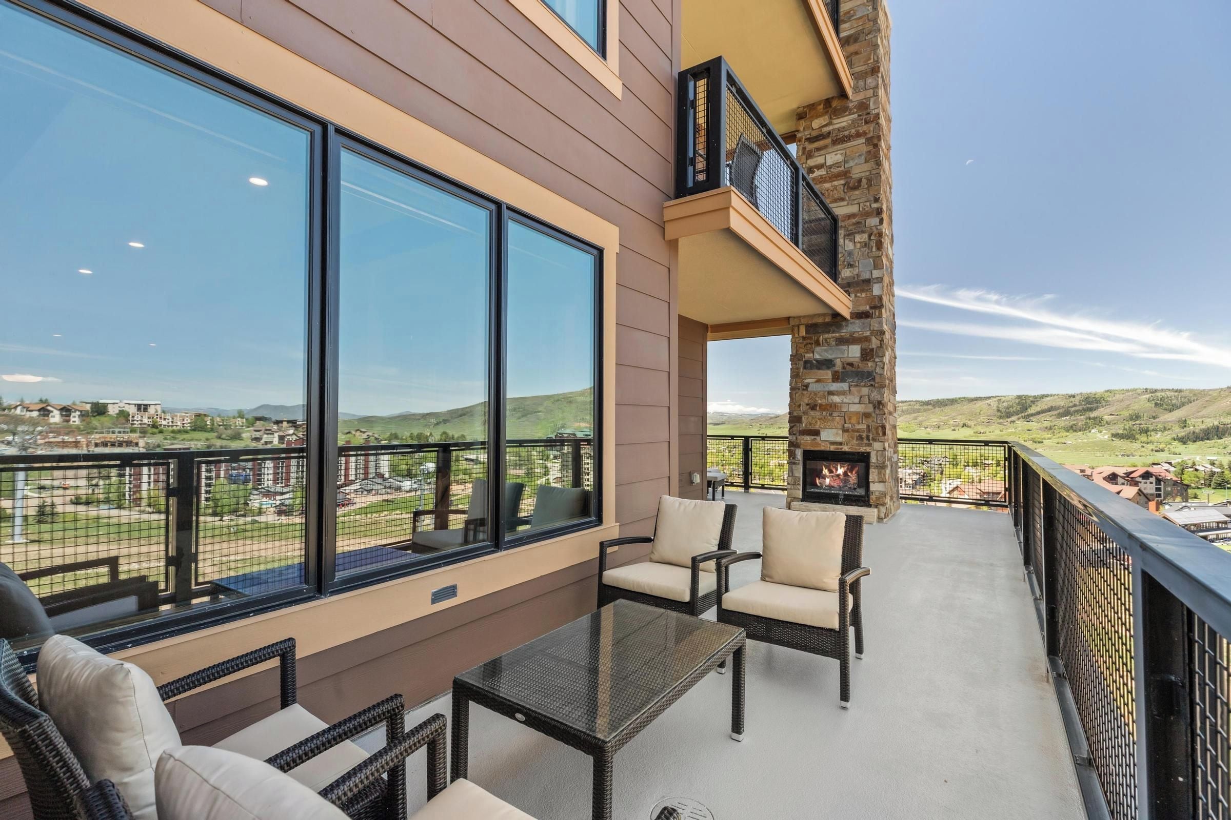 A balcony with wicker furniture and a glass table, overlooking a scenic landscape.