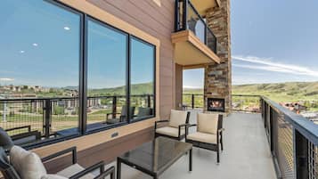 A balcony with wicker furniture and a glass table, overlooking a scenic landscape.