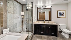 A modern bathroom with a glass-enclosed shower, a bathtub, a vanity with dark cabinets, and a toilet. - Edgemont Condominiums (Steamboat Springs)