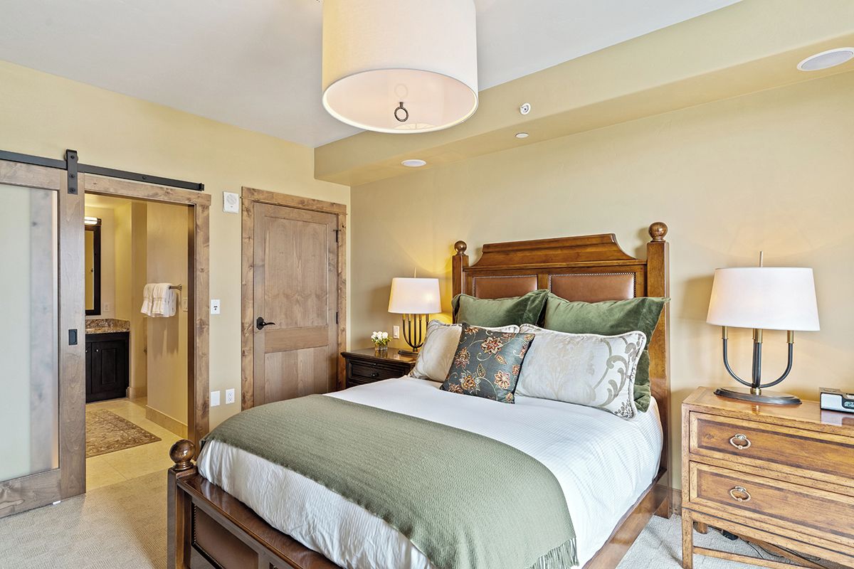 A bedroom with a wooden bed, two bedside tables with lamps, a large door, and a ceiling light fixture.