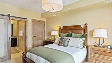 A bedroom with a wooden bed, two bedside tables with lamps, a large door, and a ceiling light fixture.