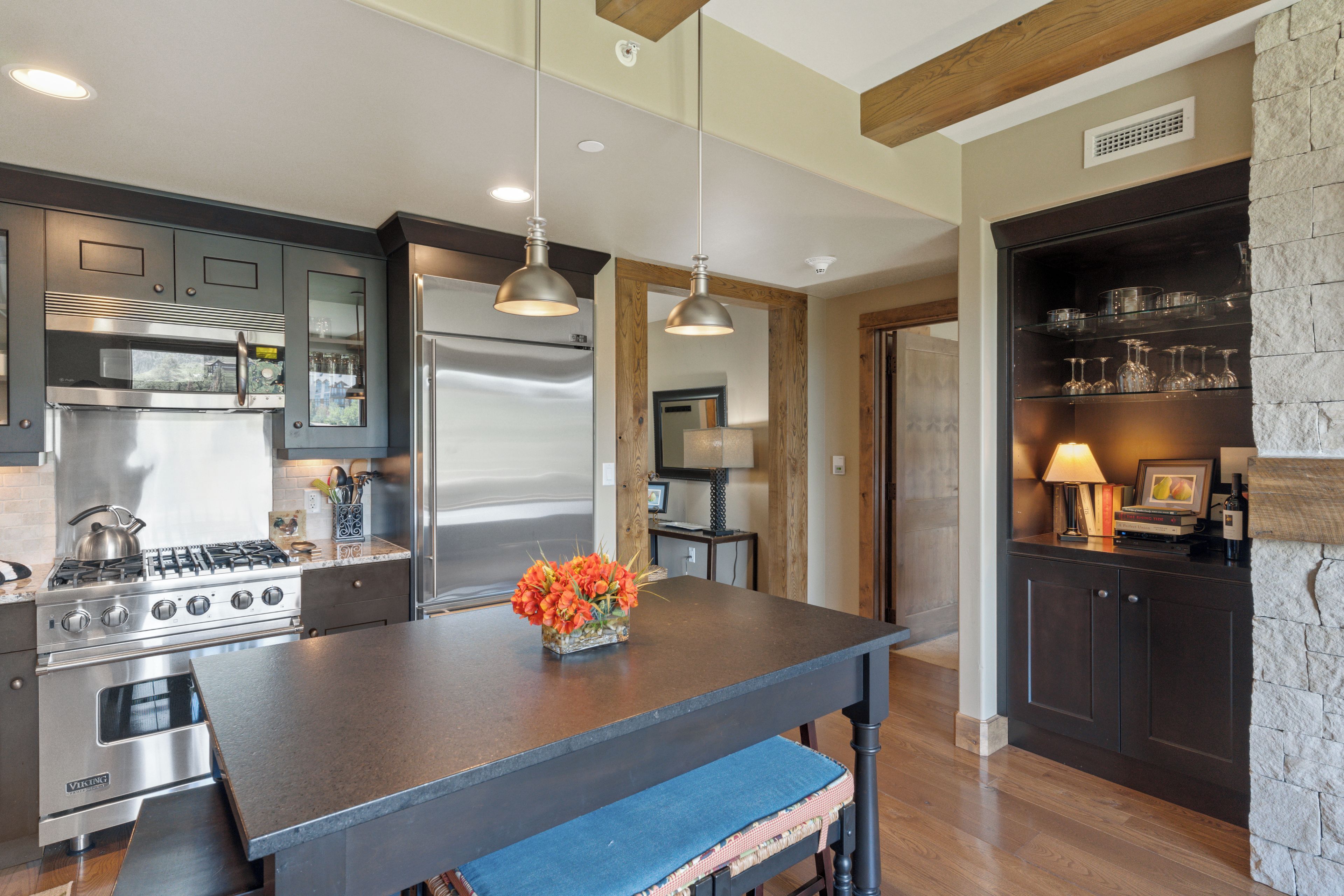 A modern kitchen with stainless steel appliances, a central island, pendant lighting, and a stone accent wall.