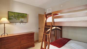 Een stapelbed met een ladder, een houten dressoir, een lamp en een schilderij aan de muur.