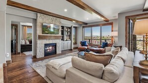 A spacious living room with a stone fireplace, comfortable seating, and large windows offering a view. - Edgemont Condominiums (Steamboat Springs)