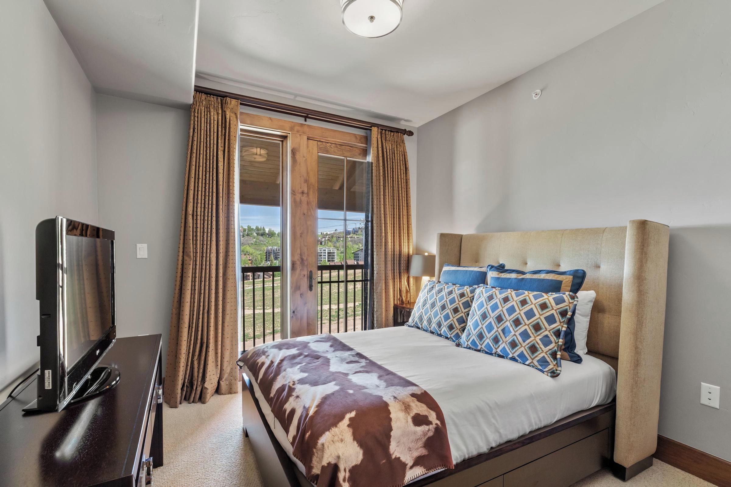 A bedroom with a bed, a TV, and a balcony with curtains.