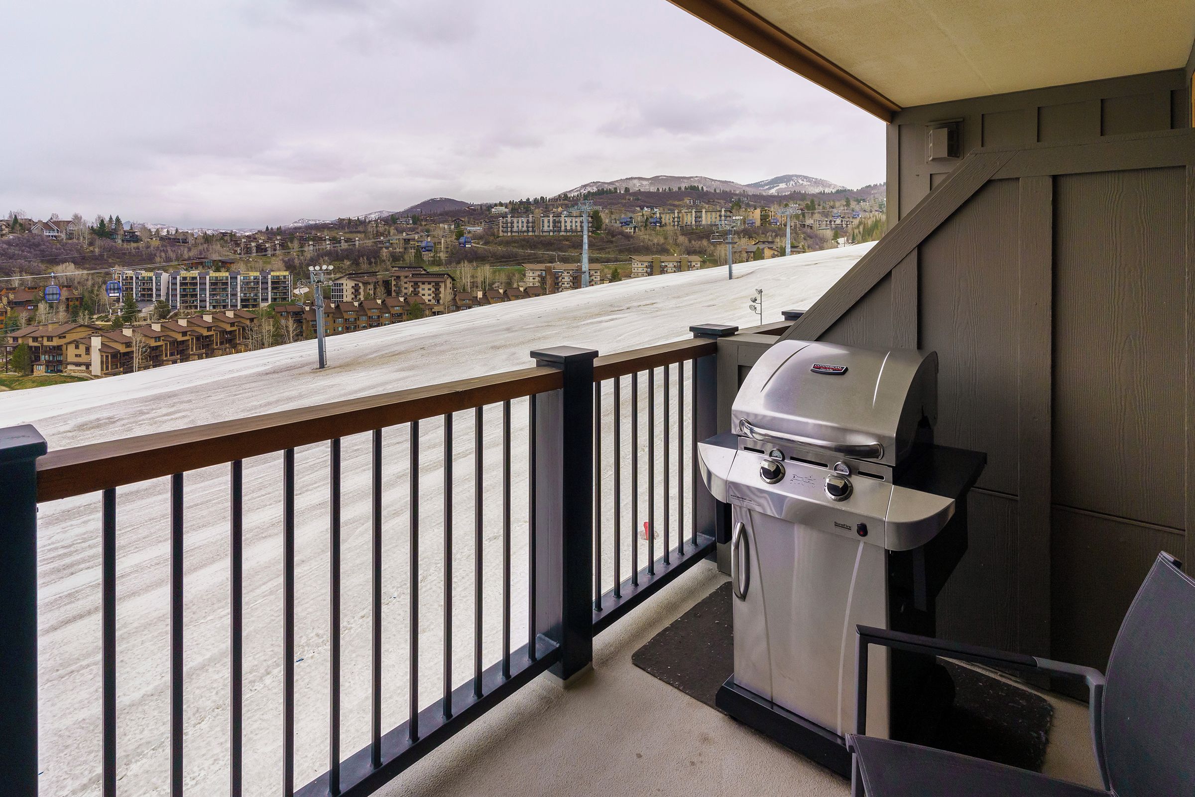 A balcony with a barbecue grill, a view of a road, and buildings in the distance.