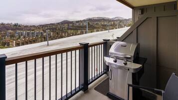 A balcony with a barbecue grill, a view of a road, and buildings in the distance.