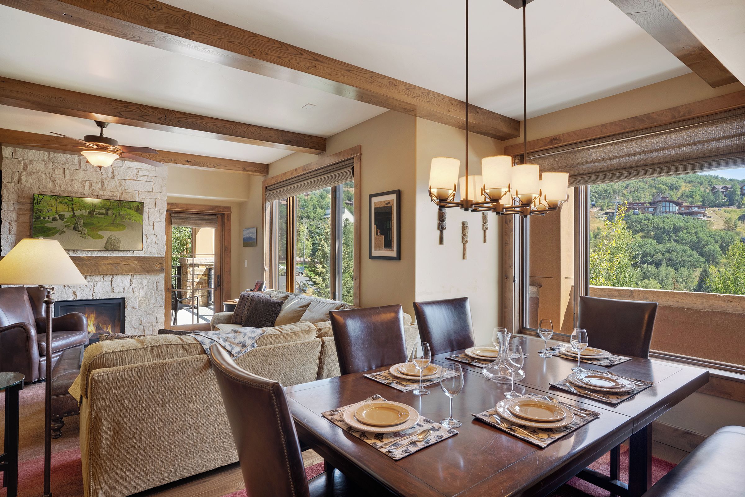 A dining area with a wooden table set for six, a fireplace, and a view of the outdoors.
