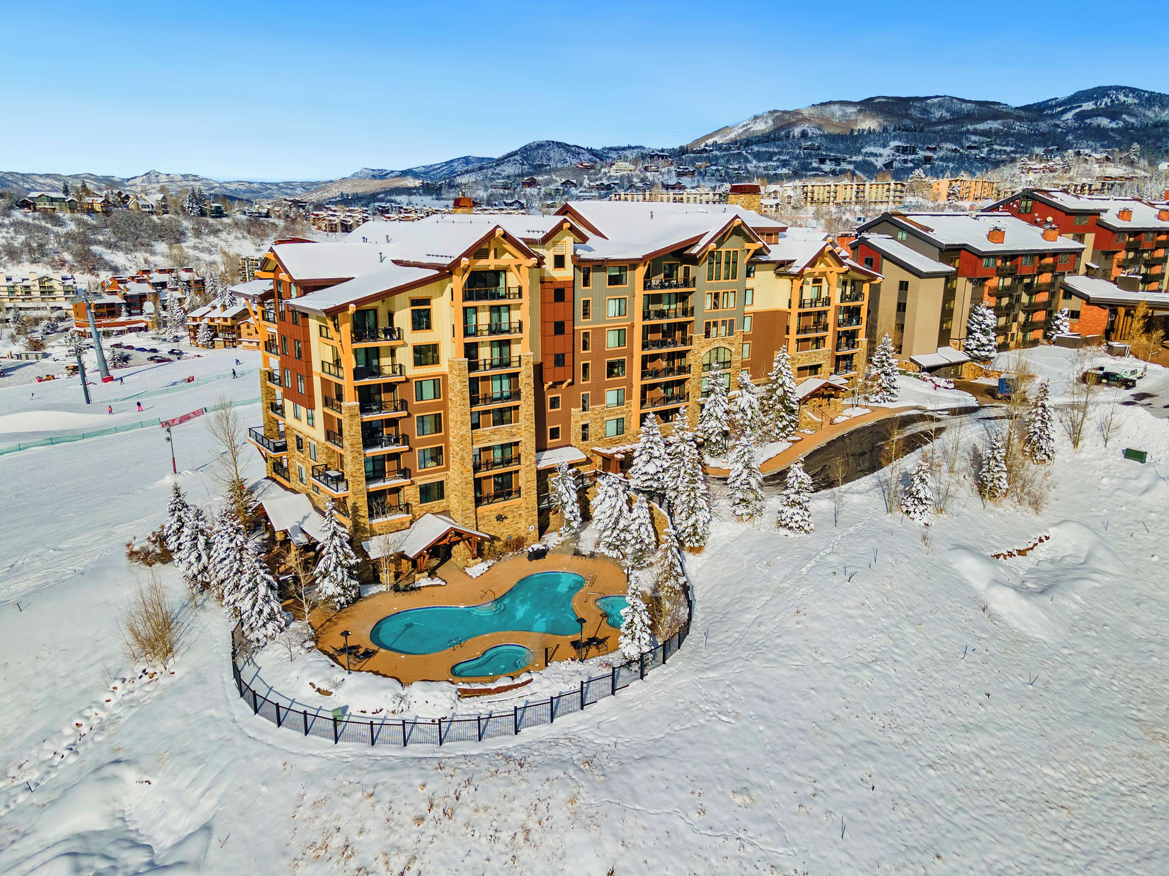 Ein mehrstöckiges Hotel mit Schwimmbad, umgeben von Schnee, vor einer Bergkulisse.