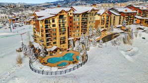 A multi-story hotel with a pool surrounded by snow, set against a mountainous backdrop. - Edgemont Condominiums (Steamboat Springs)