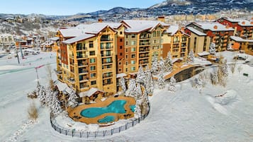 Ein mehrstöckiges Hotel mit Schwimmbad, umgeben von Schnee, vor einer Bergkulisse.
