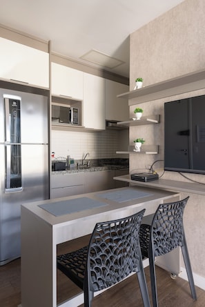 A modern kitchen with a built-in microwave, stainless steel refrigerator, and a dining area with a table and chairs. - StayHome - Centro Histórico - Gym & Pool (São Paulo)