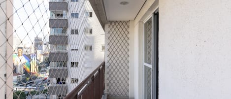 Un balcón con vista a un edificio alto, una cerca de metal y un suelo de baldosas.