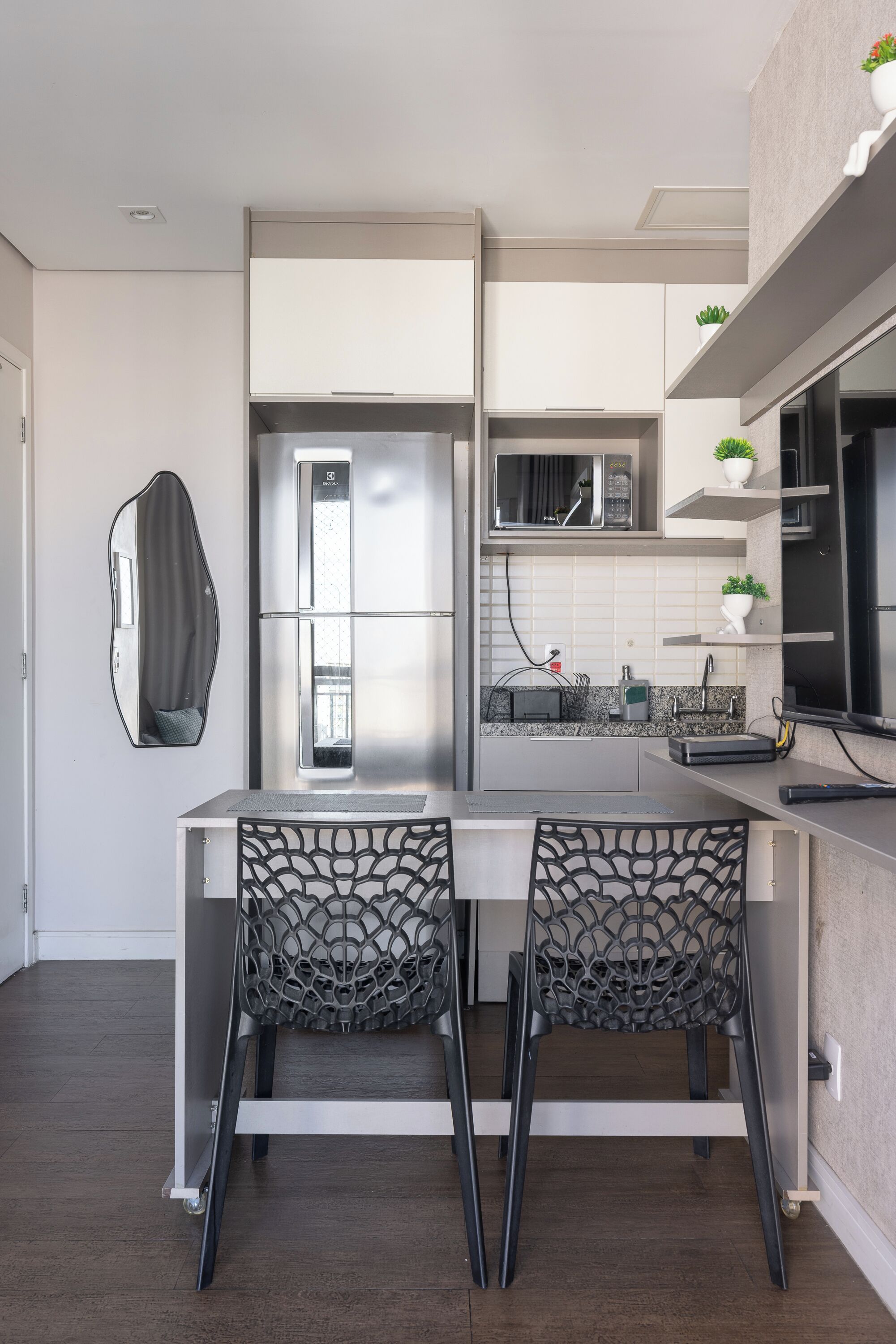 Una cocina moderna con una isla central, dos sillas, un refrigerador, un microondas y un fregadero.