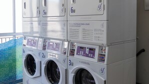 Varias lavadoras apiladas, con paneles de control y códigos QR, y un cartel que indica prohibido fumar.
